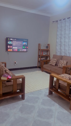 Un salon avec un téléviseur à écran plat fixé au mur, une table basse en bois, un canapé et une bibliothèque.