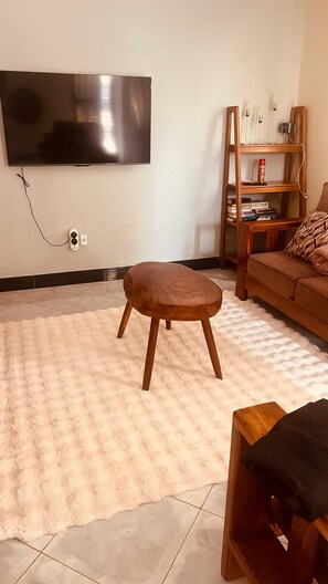 Ein Wohnzimmer mit einem an der Wand montierten Flachbildfernseher, einem Holzschemel, einer Couch und einem Bücherregal.