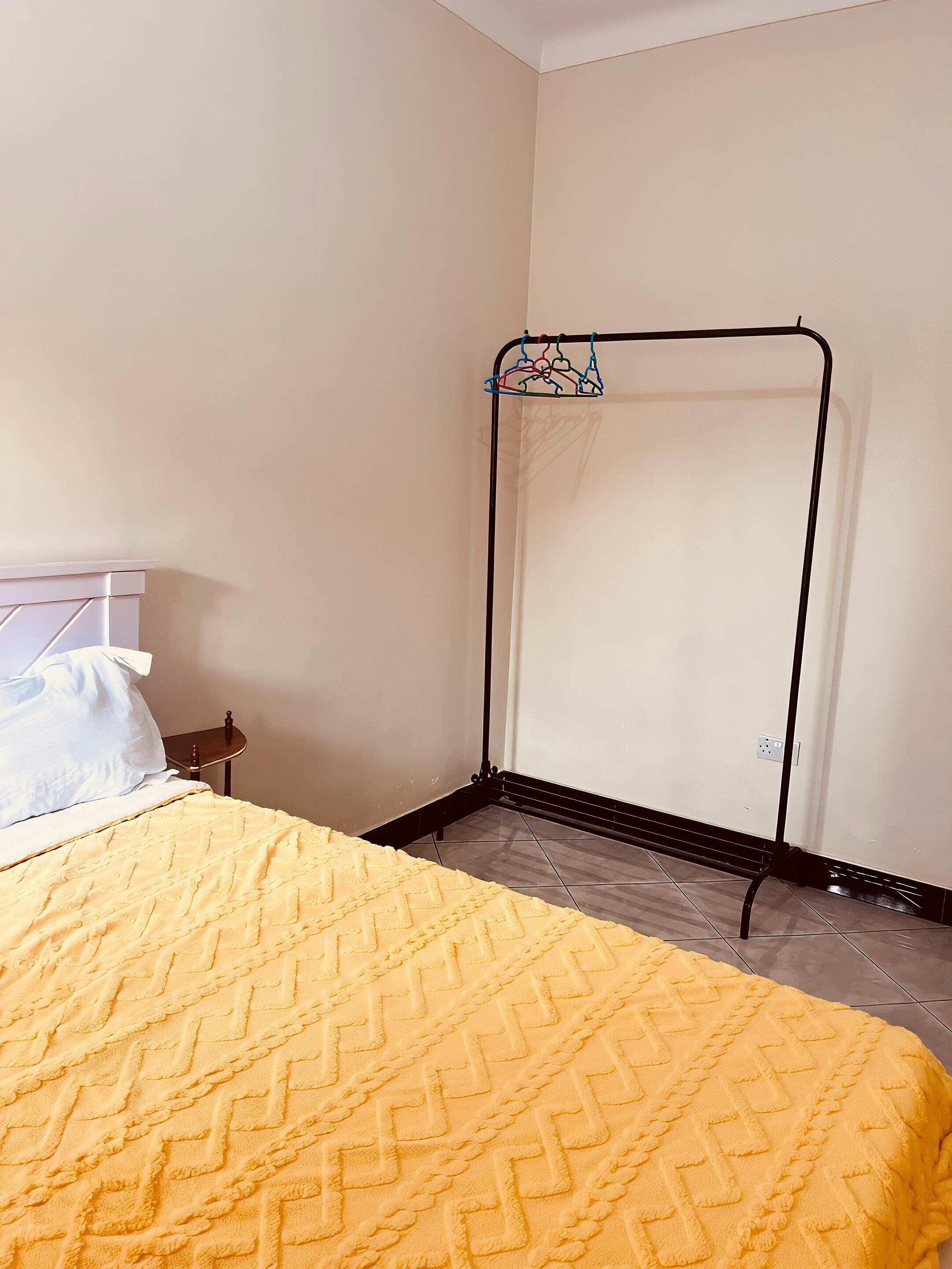Una habitación con una cama, una mesita de noche, un tendedero en la pared y suelo de baldosas.