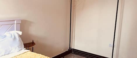 A room with a bed, a bedside table, a wall-mounted drying rack, and a tiled floor.