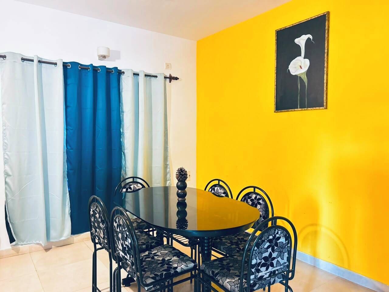 A dining area with a round table and chairs, a yellow wall, and a painting of a bird.