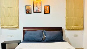Hotellihuone, jossa on sänky, kaksi yöpöytää, seinään kiinnitetty valaisin ja kolme kehystettyä taideteosta.