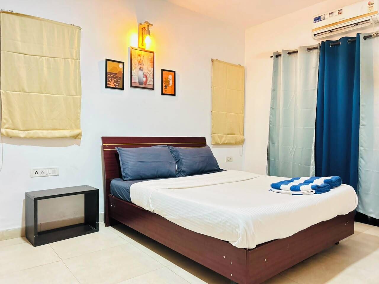 A bedroom with a bed, a bedside table, a wall-mounted air conditioner, and curtains.