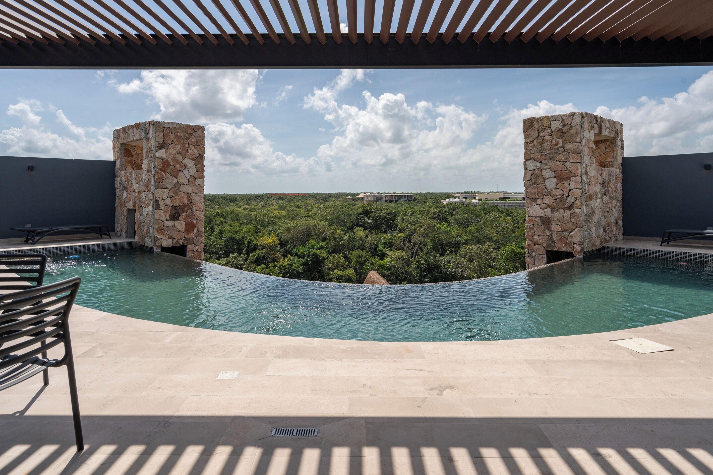 Une piscine bordée de piliers en pierre, un ciel dégagé et une vue sur la verdure.