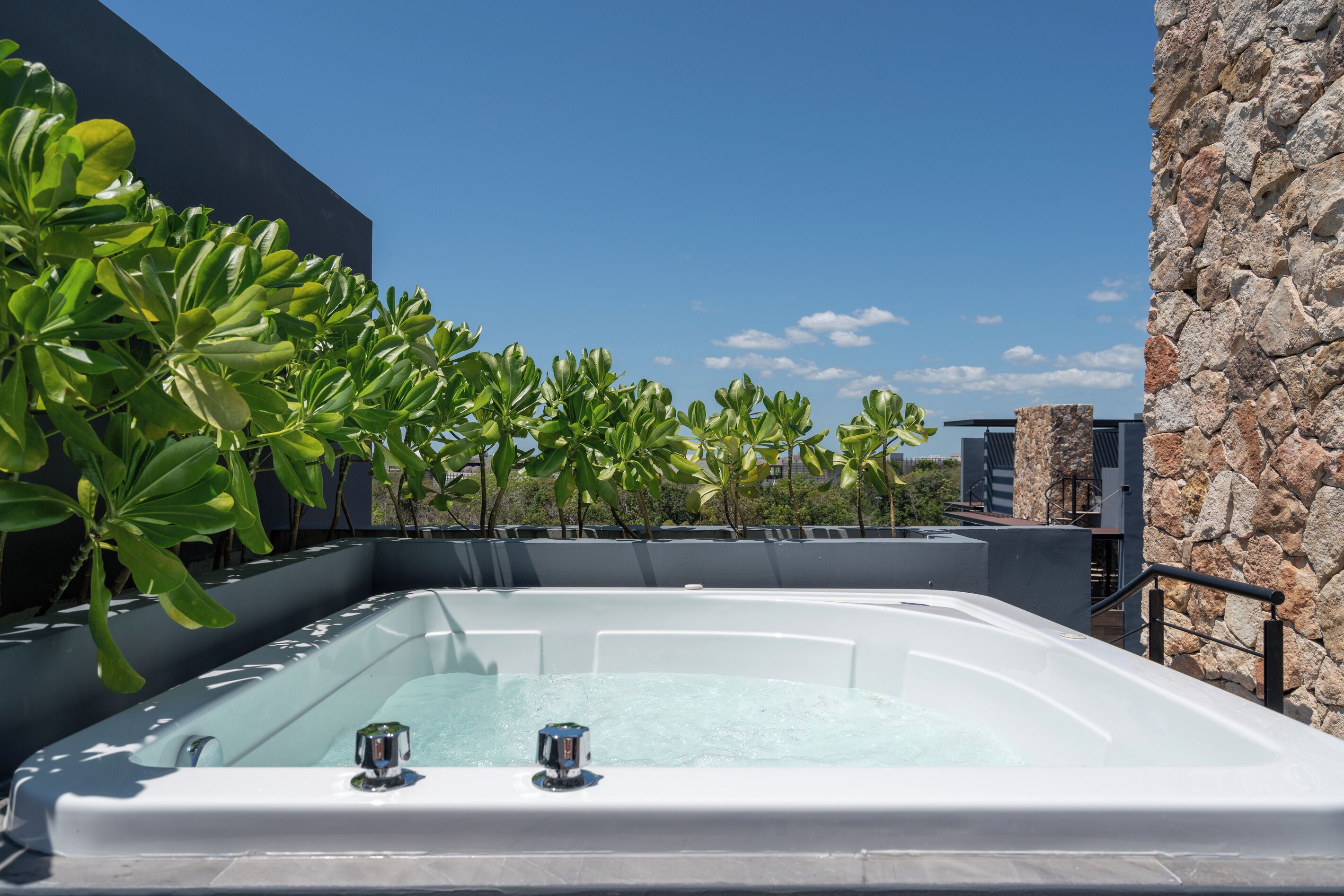 Un área de piscina en la azotea con cielo despejado, rodeada de vegetación y muros de piedra.