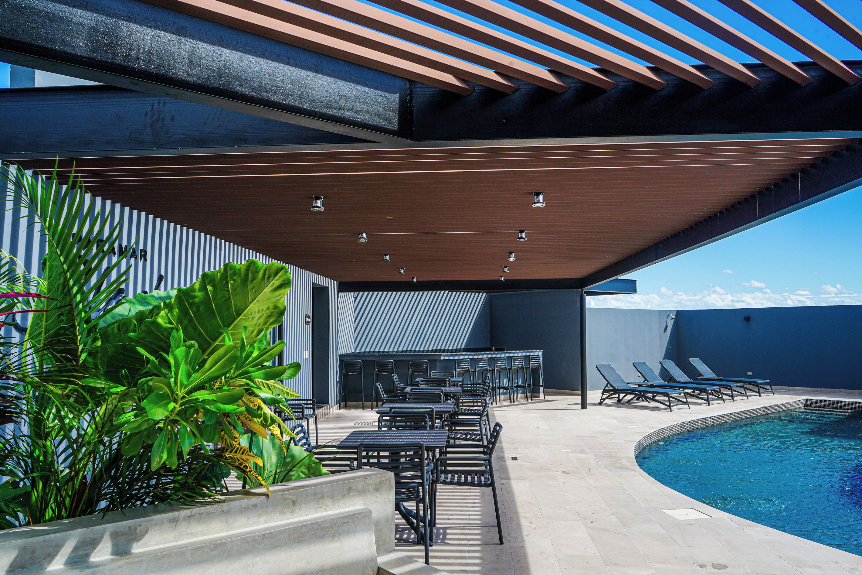 Un área de piscina al aire libre con zona de estar techada, sillas de descanso y piscina.