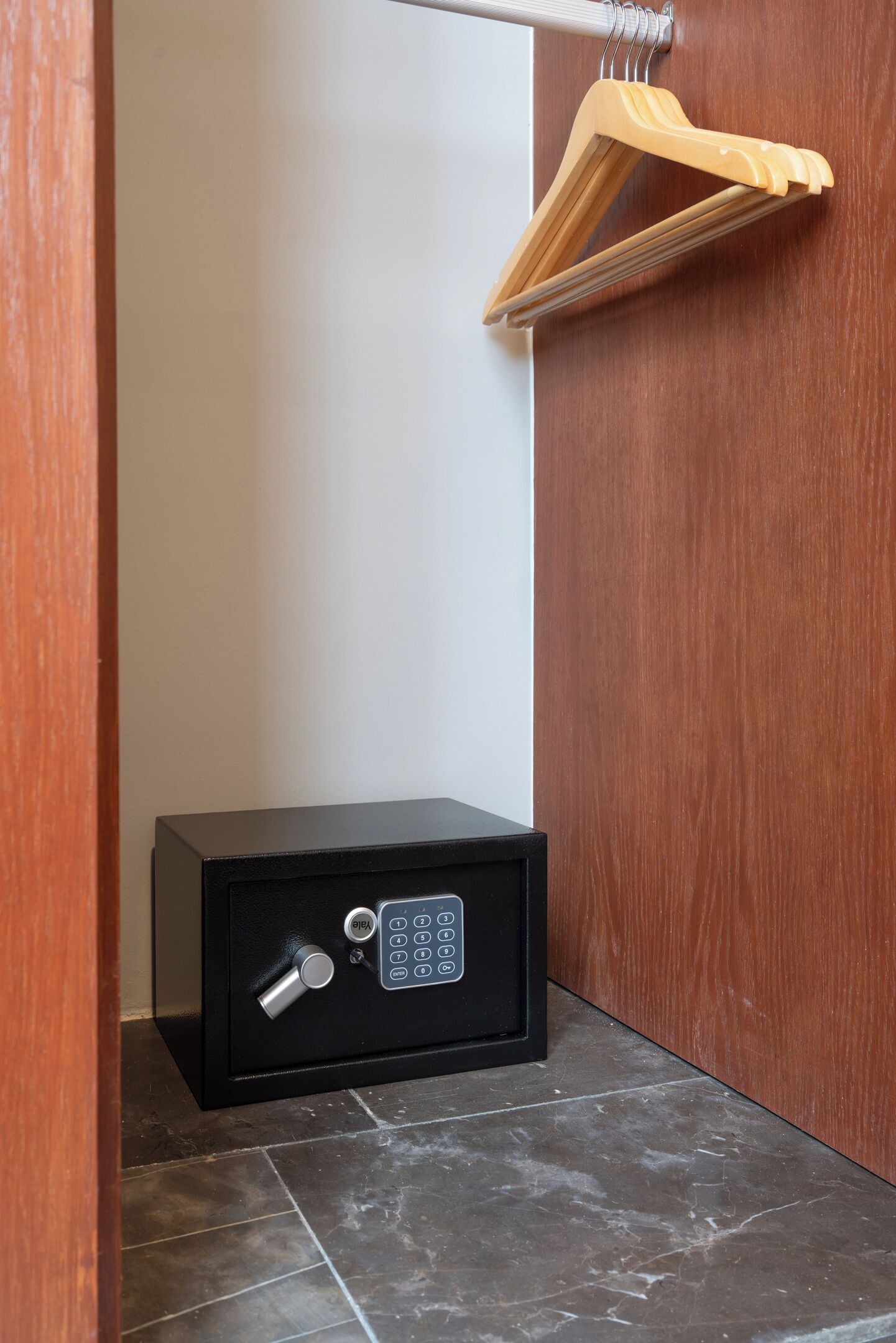 A black safe with a numeric keypad and a keyhole, placed on a tiled floor against a wooden wall.