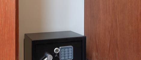 Ein schwarzer Safe mit Zahlenschloss und Schlüsselloch, auf einem gefliesten Boden vor einer Holzwand platziert.