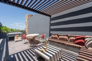 Une terrasse extérieure moderne avec un mur en pierre, une table ronde, des chaises en osier, un canapé et une bouteille de vin.
