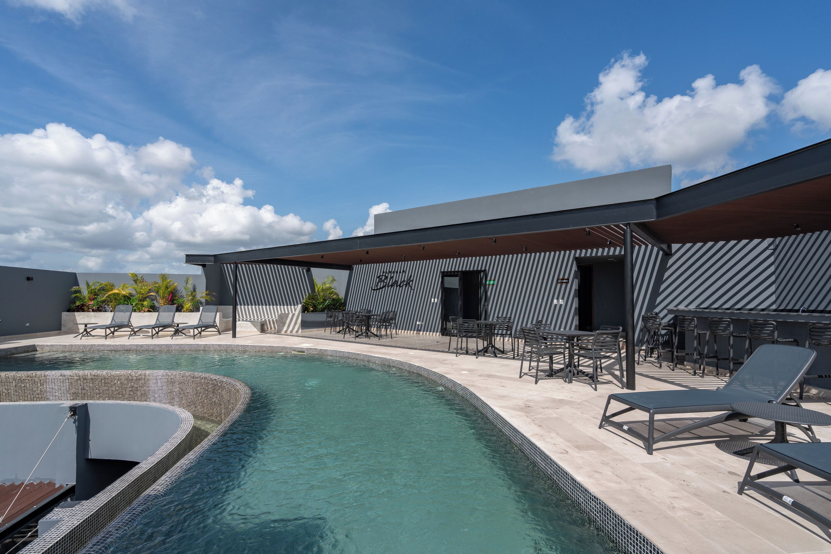A modern outdoor pool area with lounge chairs and tables, surrounded by a building with a striped facade.