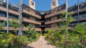 Um edifício com vários andares e um átrio central, rodeado por vegetação exuberante e um caminho de madeira.