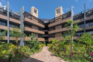 Un immeuble à plusieurs étages doté d’un atrium central, entouré d’une végétation luxuriante et d’un sentier en bois.