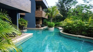 Uma área de piscina com uma piscina azul cristalina, cercada por vegetação exuberante e arquitetura moderna.