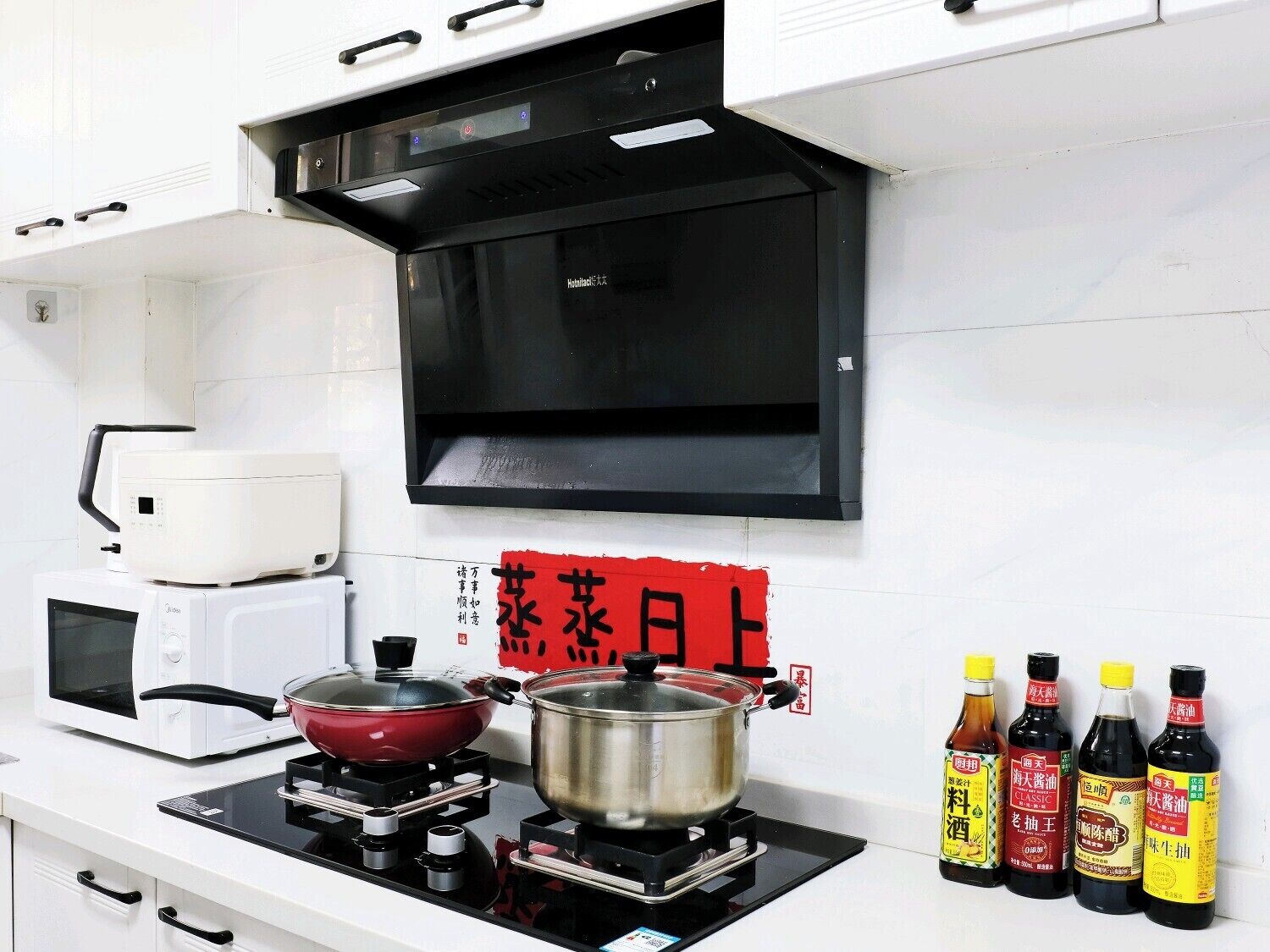 A kitchen with a microwave, stove, pots, and bottles of sauces.