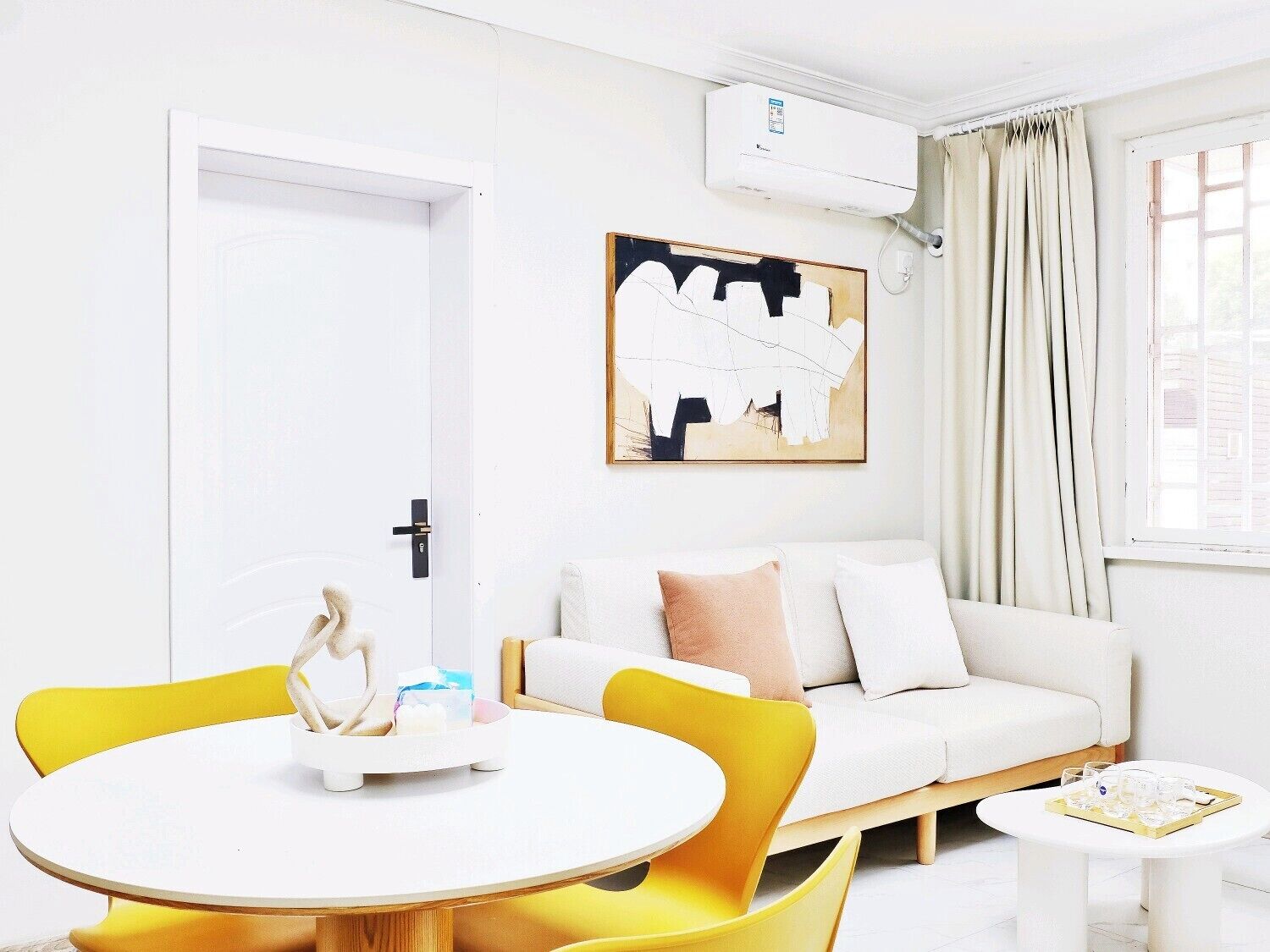 Uma sala de estar moderna com um sofá branco, poltronas amarelas, uma mesa redonda e um quadro na parede.