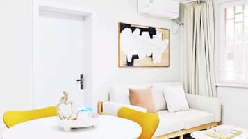 Uma sala de estar moderna com um sofá branco, poltronas amarelas, uma mesa redonda e um quadro na parede.
