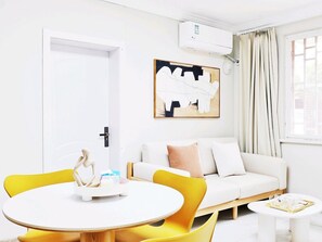 A modern living room with a white sofa, yellow chairs, a round table, and a painting on the wall. - Shanghai Hills & Linghu's Cozy 3-BedHome (Shanghai)