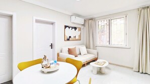 Uma sala de estar moderna com um sofá branco, uma mesa de jantar redonda e uma janela com cortinas.