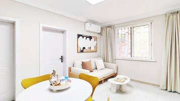 A modern living room with a white sofa, a round dining table, and a window with curtains.