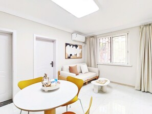 A modern living room with a white sofa, a round dining table, and a window with curtains. - Shanghai Hills & Linghu's Cozy 3-BedHome (Shanghai)