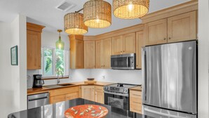 Eine moderne Küche mit Holzschränken, Edelstahlgeräten, einer schwarzen Arbeitsplatte und einer zentralen Kochinsel mit einer dekorativen Schüssel.