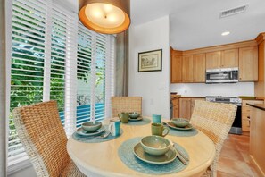 A dining area with a round table, woven chairs, and a view through large windows. - Sunrise Lagoon by Duncan Real Estate (Anna Maria)