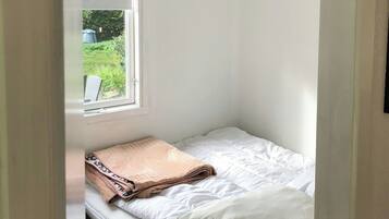 Una habitación pequeña con cama individual, ventana y vistas al exterior con vegetación.