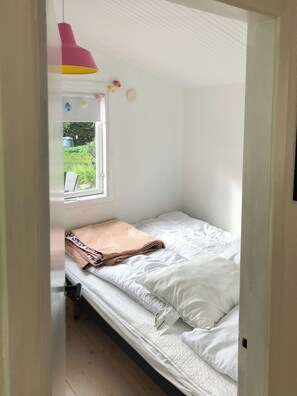 Ein kleines Zimmer mit einem Einzelbett, einem Fenster, einer hängenden rosa Lampe und Blick auf Grünflächen.