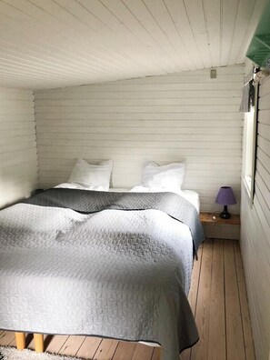 Una cama individual con un edredón gris, almohadas blancas y suelo de madera.