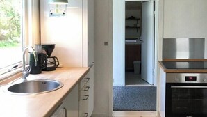 Una cucina compatta con lavello, piano di lavoro e fornelli. Si apre una porta verso un'altra stanza.
