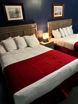 Habitación de hotel con dos camas, una mesita de noche con lámpara y cuadros en la pared.