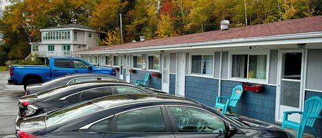 A row of cars parked in front of a motel with a row of chairs outside.