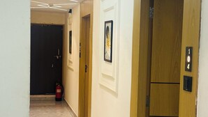 A corridor with a fire extinguisher, a framed picture on the wall, and a door with a number plate. - Hotel sun town (Ahmedabad)