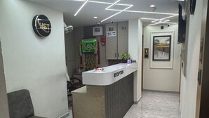 A reception area with a reception desk, a grey sofa, and a tiled floor. - Hotel sun town (Ahmedabad)