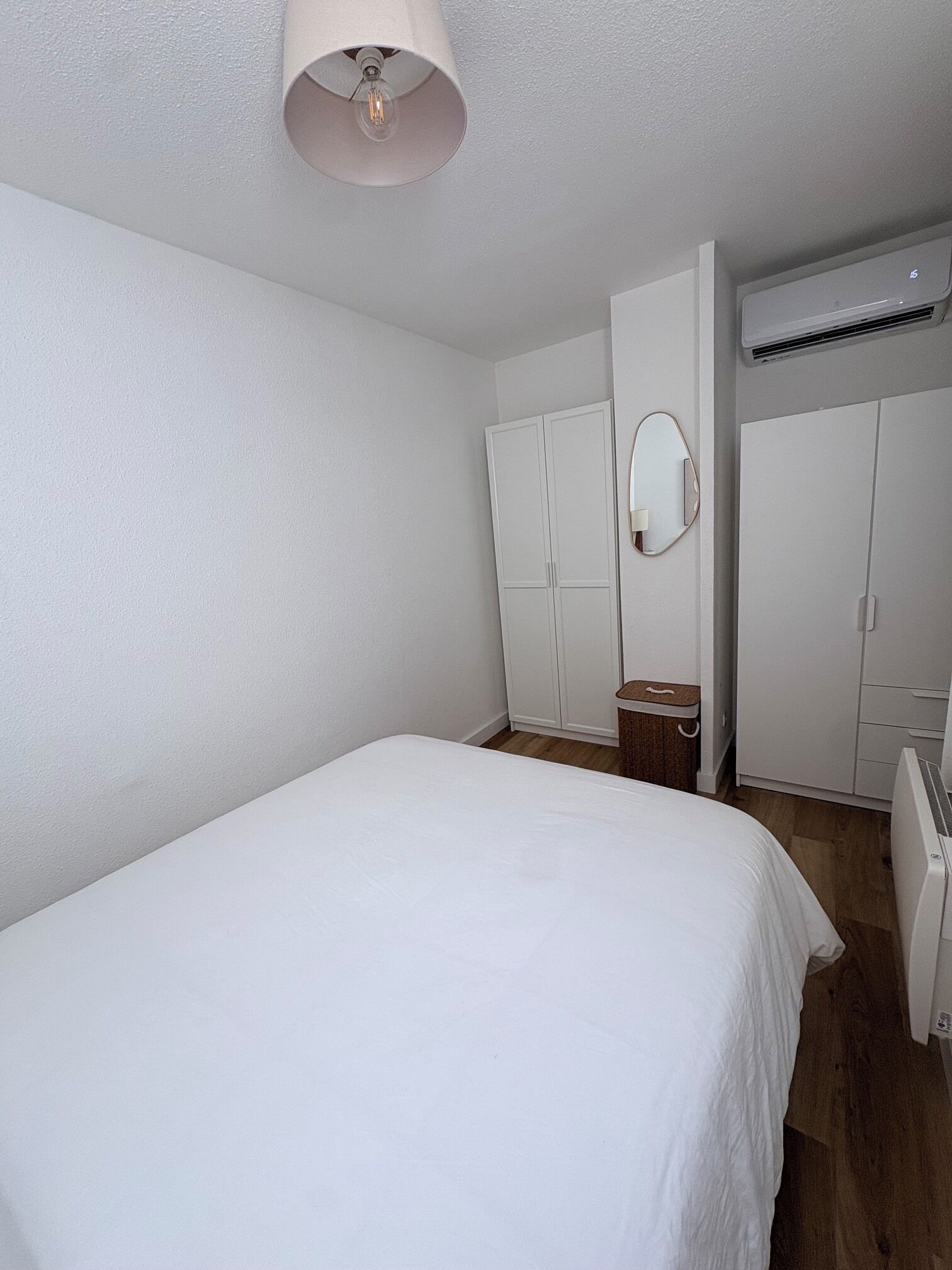 Un dormitorio con cama, armario, espejo y aire acondicionado.
