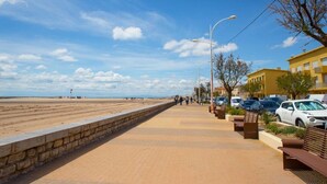 Un paseo marítimo con muro de piedra, bancos y coches estacionados.