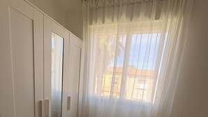 Un dormitorio con cama, armario y ventana con cortinas.