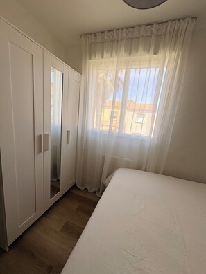 Ein Schlafzimmer mit Bett, Kleiderschrank und einem fenster mit Vorhängen.
