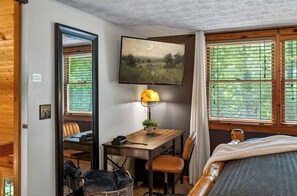 Ein Zimmer mit einem Bett, einem Schreibtisch mit Lampe, einem Sessel, einem Spiegel und einem Bild an der Wand.