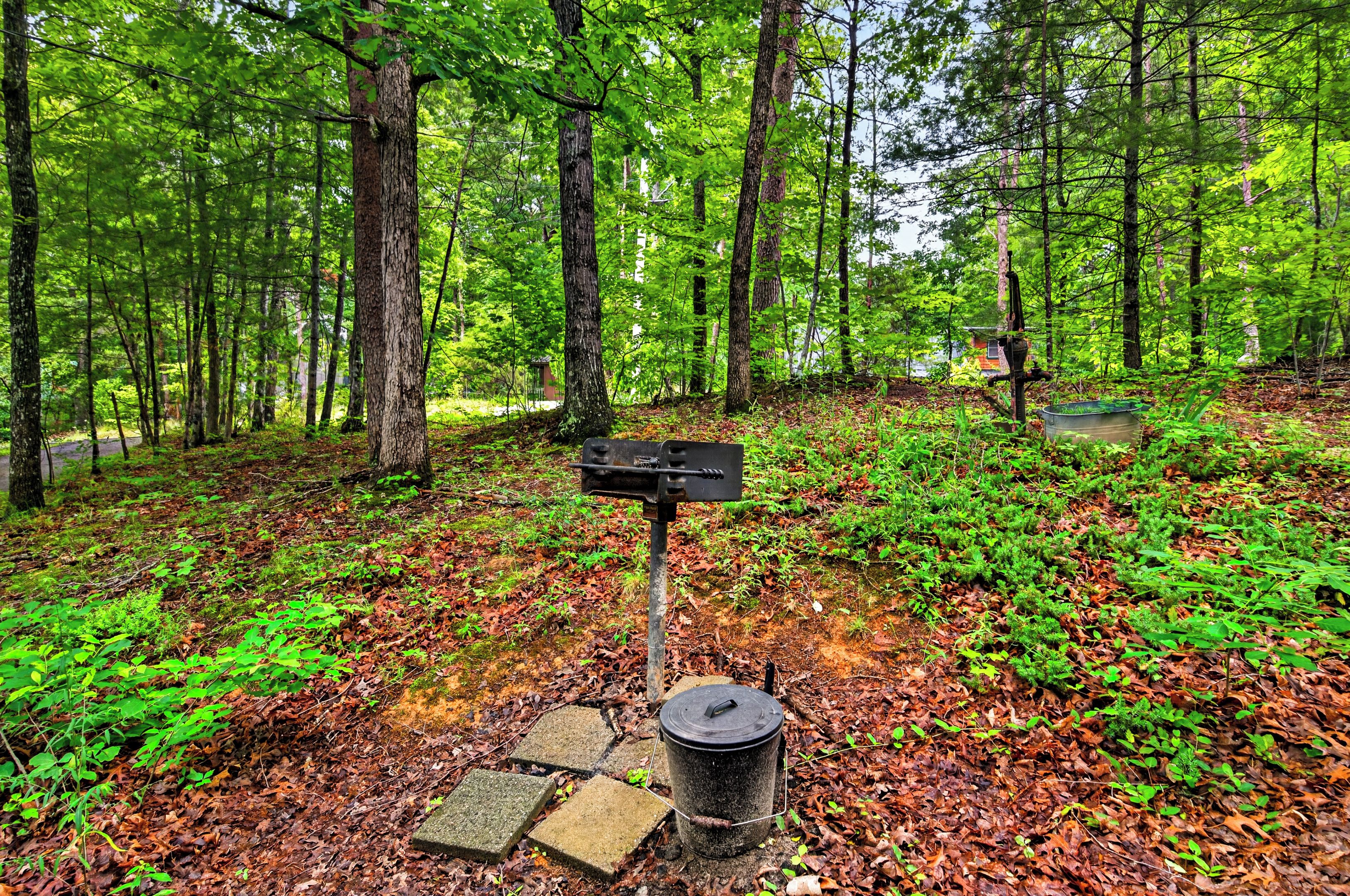 A forested area with a metal signpost and a trash can on a stone base.