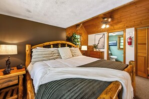 Quarto com estrutura de madeira, uma cama grande, mesa de cabeceira com abajur e extintor fixado na parede.