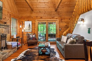 A cozy cabin interior with a stone fireplace, leather armchair, and a large window overlooking greenery. - Smoky Mtn Retreat Hot Tub Fire Table EV Pets OK (Sevierville)