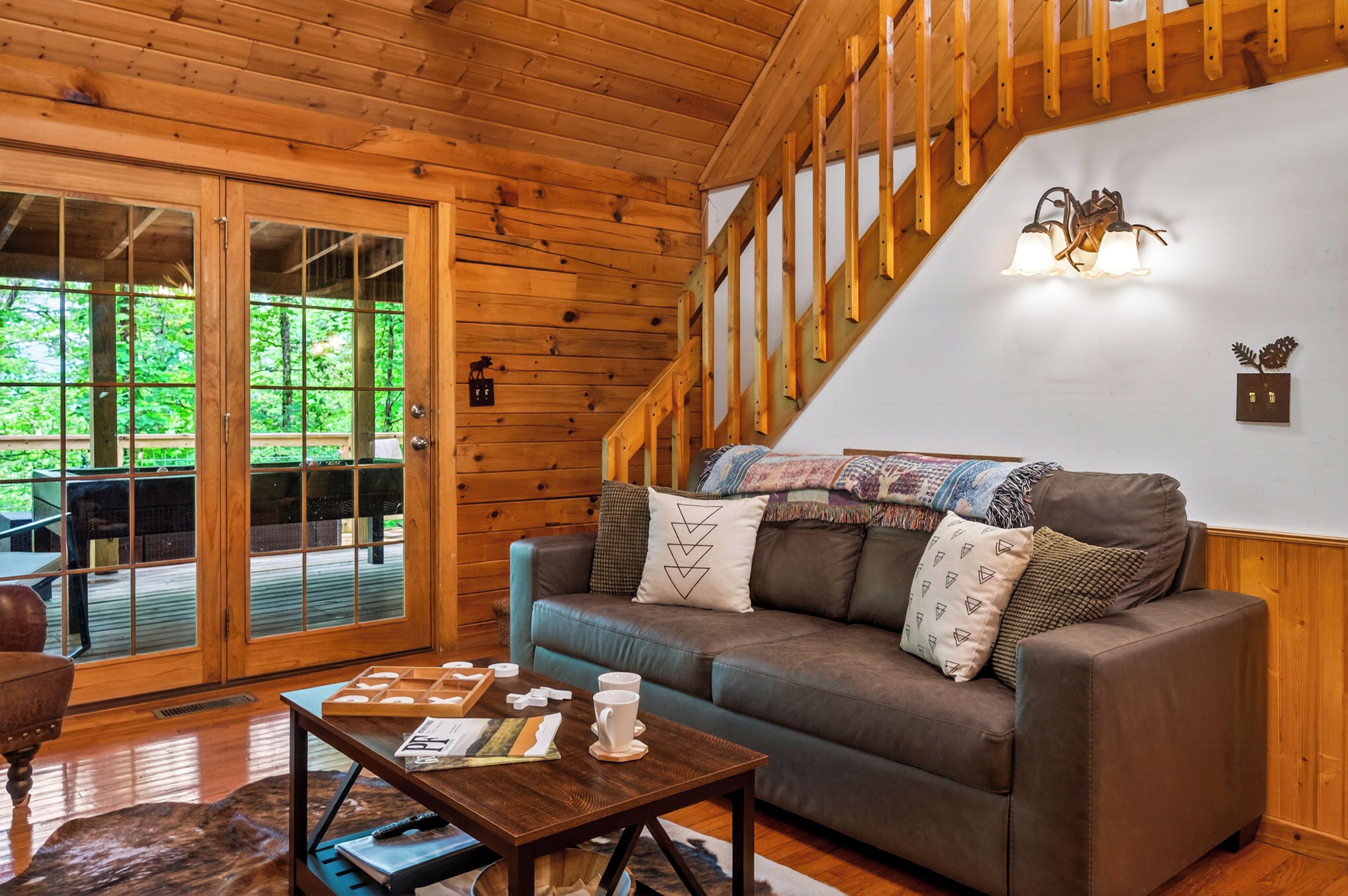 A wooden interior with a sofa, a table with books and a cup, and a view through a glass door.