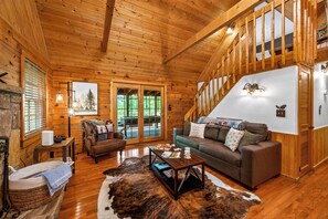 A log cabin interior with a fireplace, a sofa, a coffee table, and a cowhide rug. - Smoky Mtn Retreat Hot Tub Fire Table EV Pets OK (Sevierville)