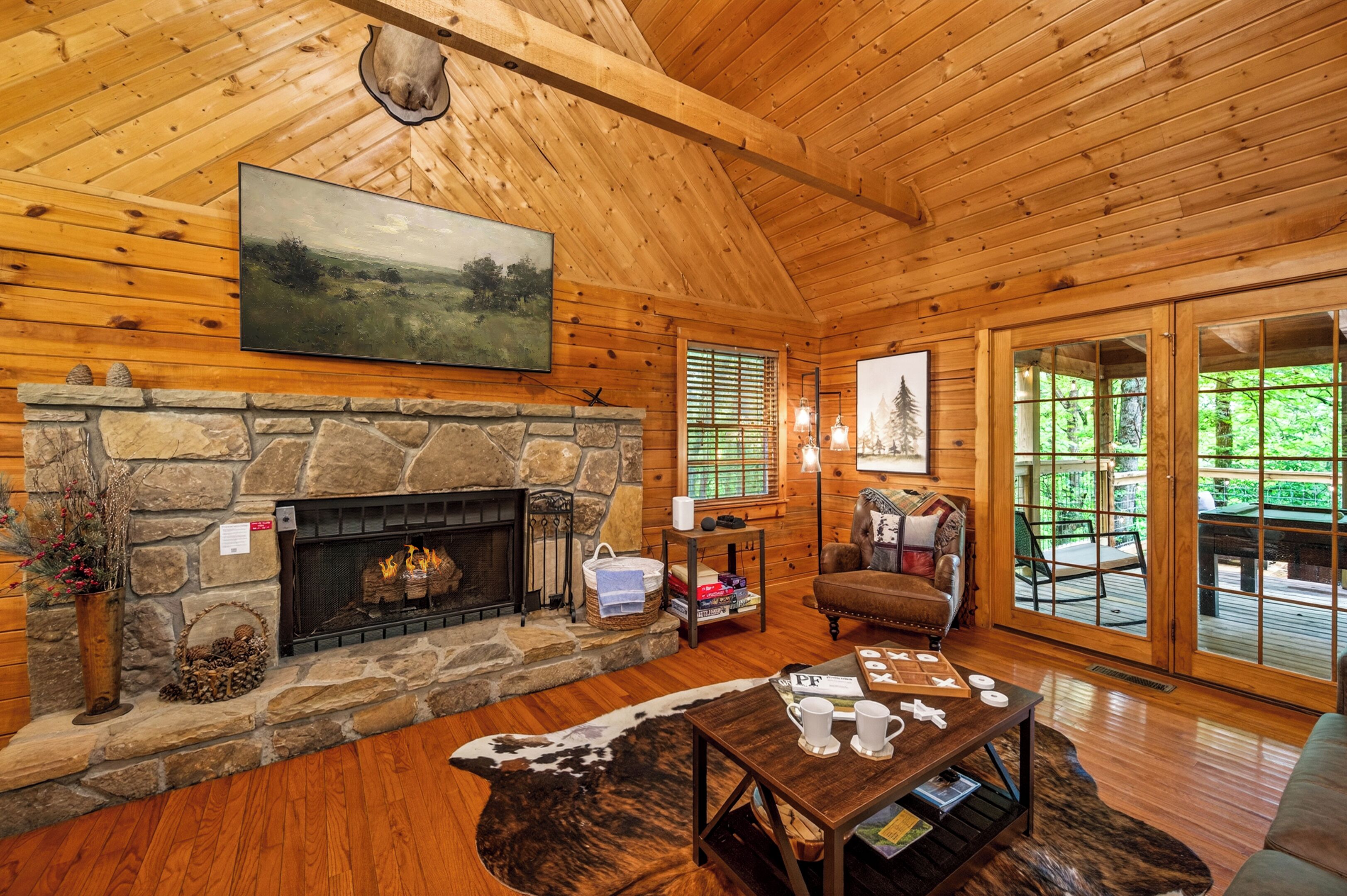 A log cabin interior with a stone fireplace, a mounted painting, and a view through the glass doors.