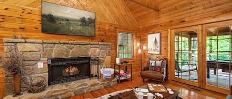 A log cabin interior with a stone fireplace, a mounted painting, and a view through the glass doors.