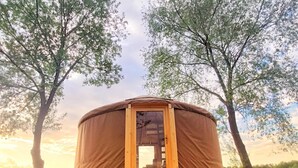 Una estructura circular de madera con una puerta, rodeada de césped y árboles.