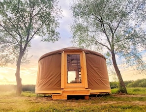 Una estructura circular de madera con una puerta, rodeada de césped y árboles.