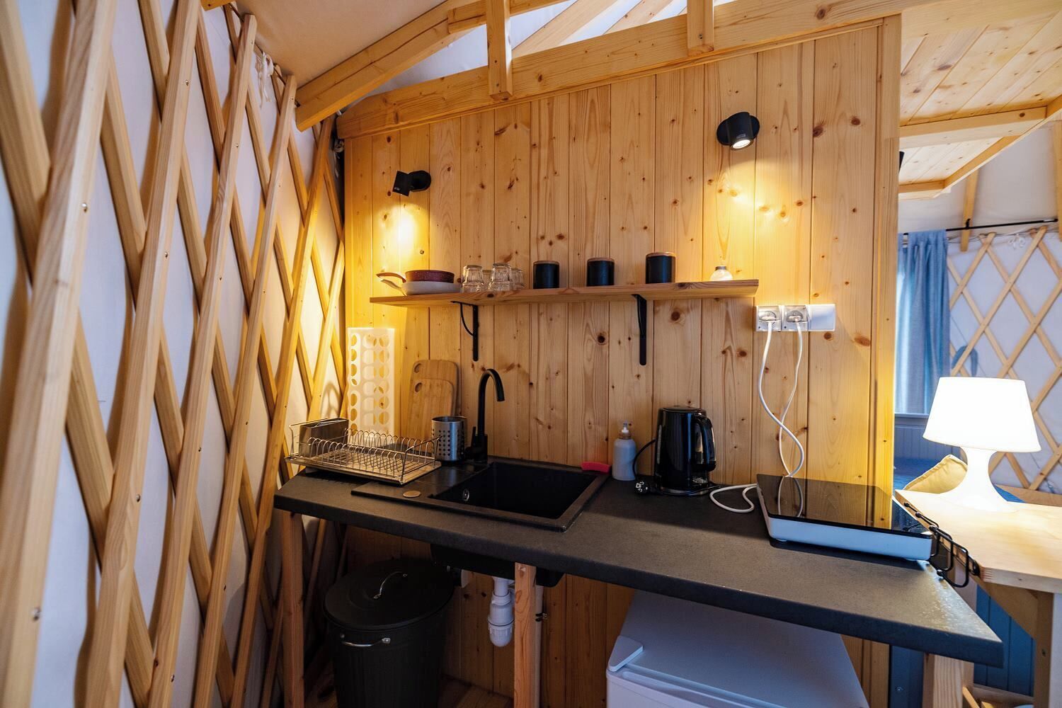 Une cuisine compacte avec des murs en bois, un plan de travail noir, un évier, une machine à café et une poubelle.