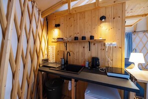 A compact kitchen with wooden walls, a black countertop, a sink, a coffee maker, and a trash bin.